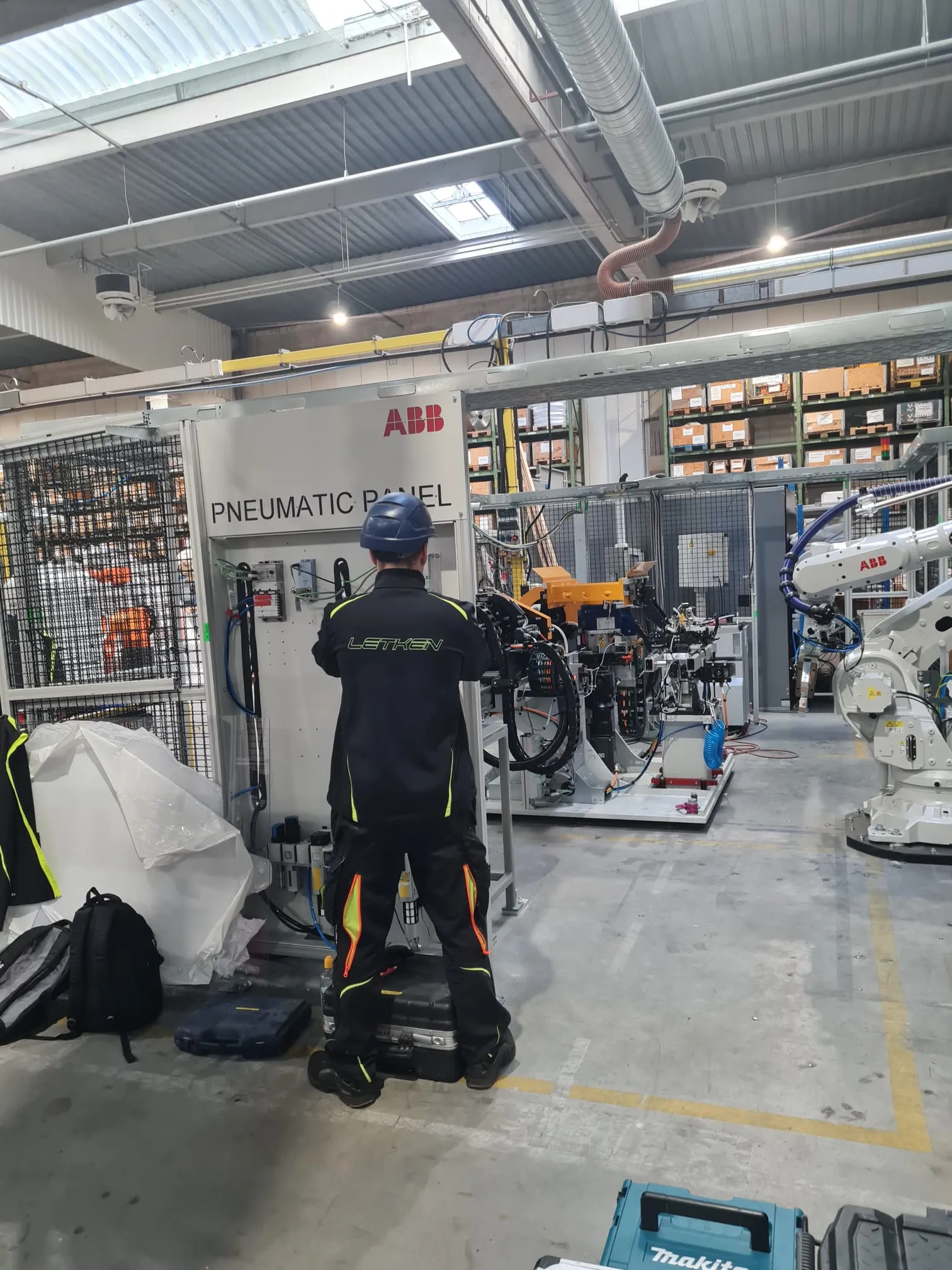 Technician working on an ABB pneumatic panel beside a robot