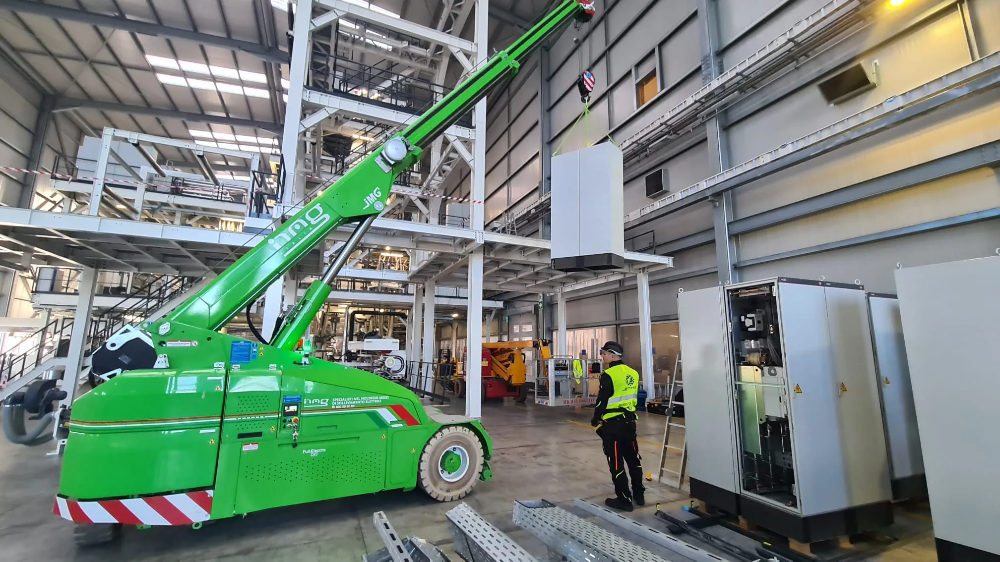 Indoor crane lifting a grey electrical cabinet into place