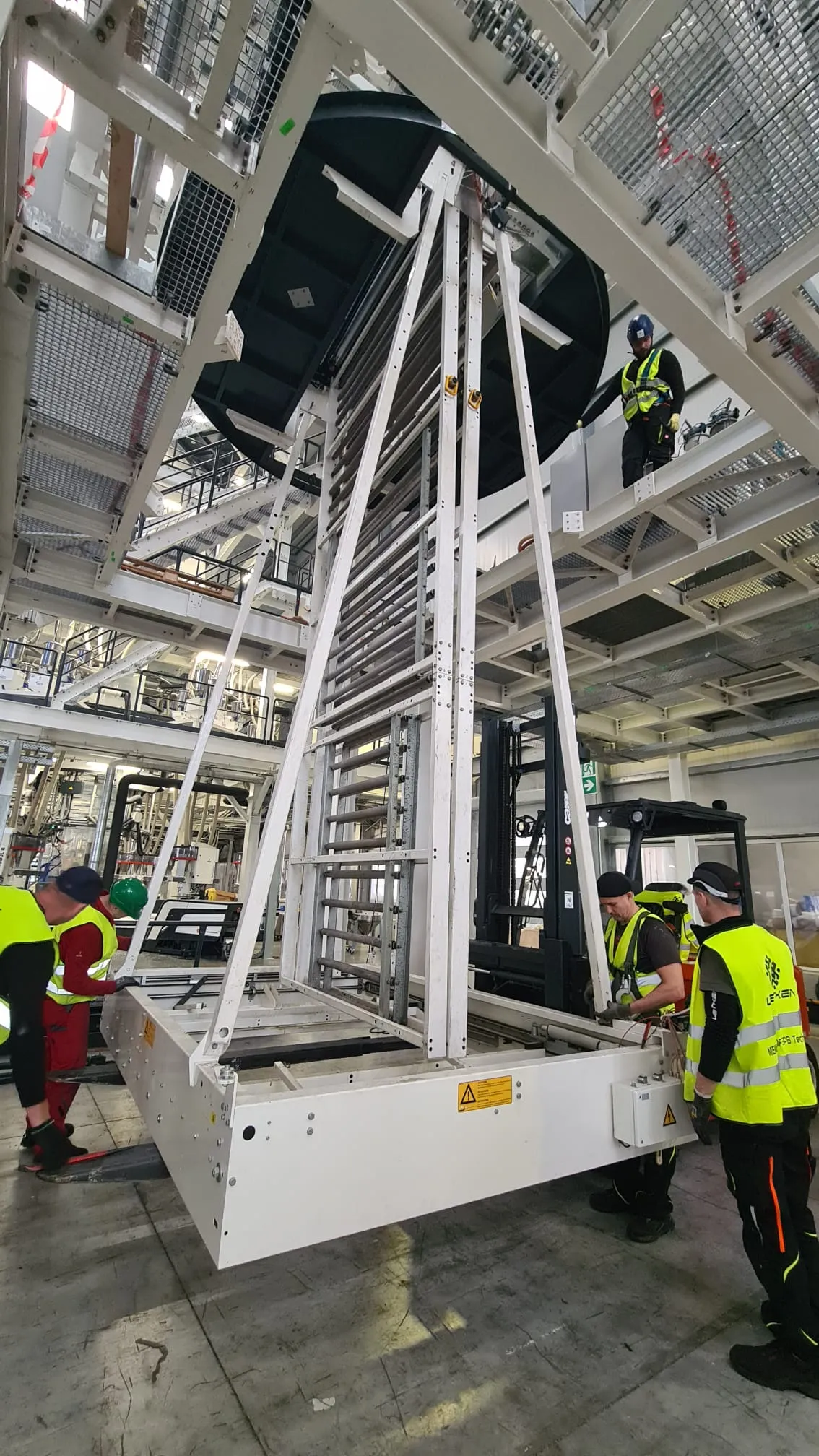 Team moving a tall machine frame with a forklift