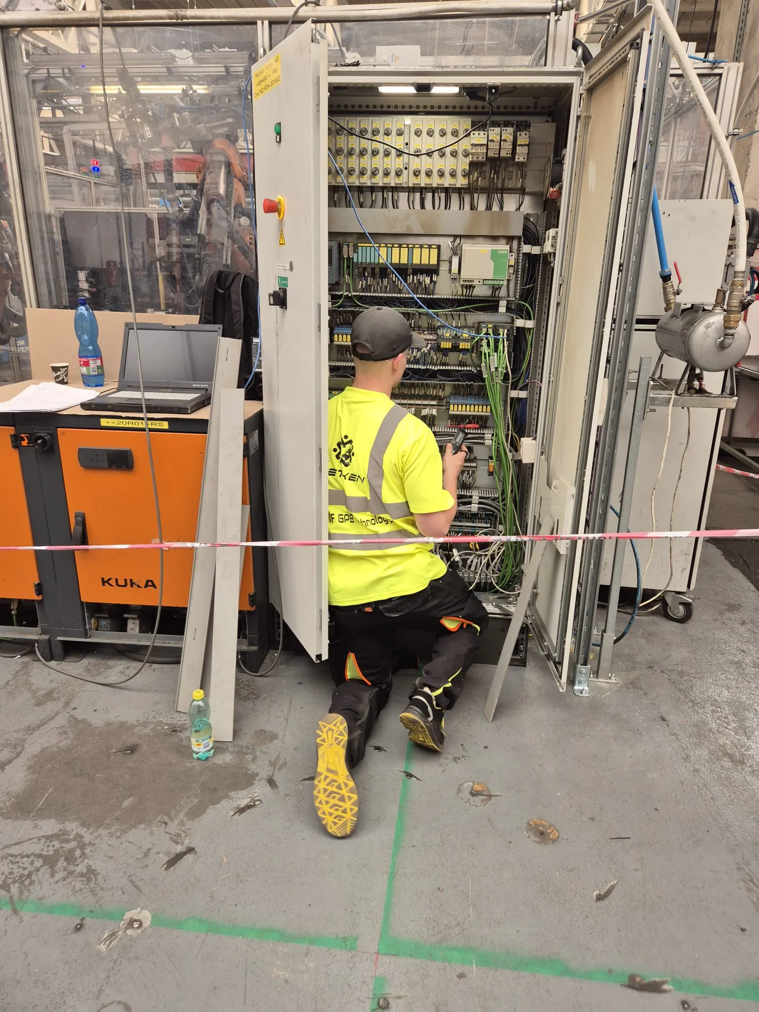 Technician commissioning a PLC cabinet beside a KUKA robot